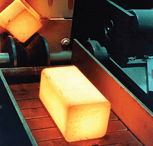 Preheated steel forging billet moving out of the furnace on a conveyor